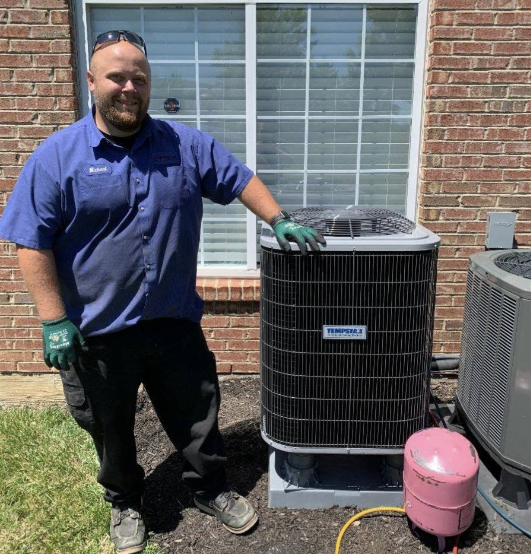 Hauser Air technician standing beside a Tempstar outdoor air conditioning unit at a brick home in Cincinnati, OH.